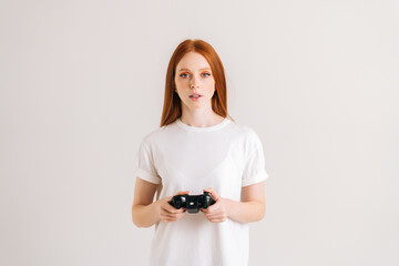 Studio portrait of attractive young woman playing video game with controller looking at camera on white isolated background. Happy lady using joystick on console enjoying online game.