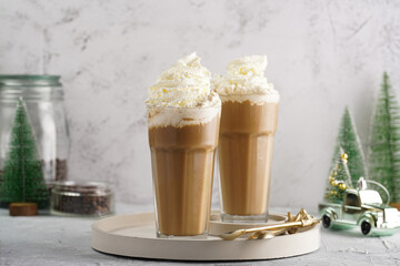 Two tall glasses with cold coffee drink frappe - iced cappuccino with whipped cream, christmas decoration and trees