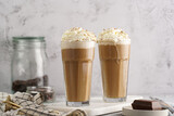 Two tall glasses with cold coffee drink frappe - iced cappuccino with whipped cream on a marble board
