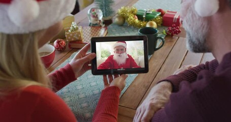 Canvas Print - Caucasian couple with santa hats using tablet for christmas video call with santa on screen