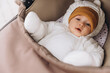 © Ananass - portrait of a cute baby dressed in a warm jumpsuit and hat lying in a stroller and looking at the camera