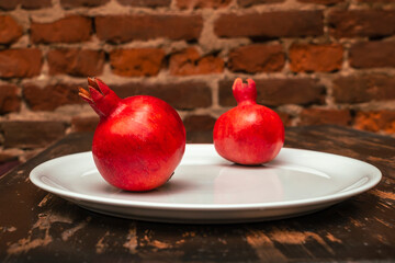 Canvas Print - Two fruit juicy Spanish pomegranate on porcelain plate on a red brick wall background.