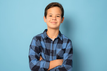 Wall Mural - Smiling boy wearing plaid shirt with arms folded standing over blue background.