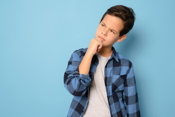 Wall Mural - Pensive boy wearing plaid shirt standing isolated over blue background.