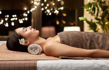 Poster - wellness, beauty and relaxation concept - young woman lying at spa or massage parlor over christmas lights on window background