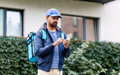 Wall Mural - food shipping, profession and people concept - indian delivery man with thermal insulated bag and smartphone on city street