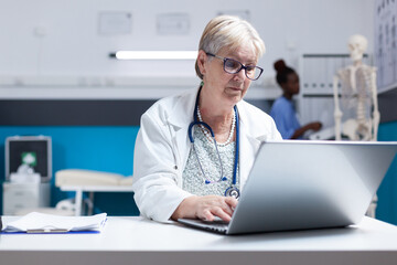 Wall Mural - Portrait of physician with stethoscope using laptop to work on healthcare at clinic. Woman doctor working with computer and technology to do prescription treatment analysis for examination.