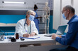© DC Studio - Woman doctor with face mask taking notes on papers at medical consultation with man. Physician signing clipboard files for healthcare treatment and medicine during covid 19 pandemic