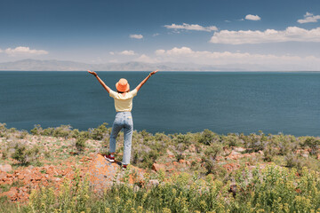 Wall Mural - A happy woman raised her hands in delight at the wonderful views of the famous Lake Sevan in Armenia