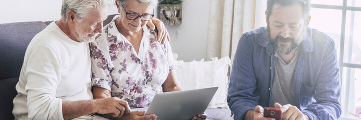 Horizontal banner header with adult and senior family together using modern devices as mobile phone and laptop computer. Concept of password security and modern people enjoying technology online