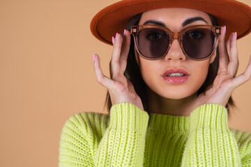 Fashionable stylish woman on a beige background in a sweater and a hat and sunglasses with brown glasses posing