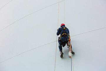 Male workers control rope down height tank rope access inspection of thickness shell plate storage tank.