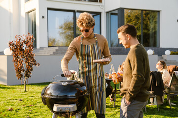 White young men cooking during barbeque in autumn garden