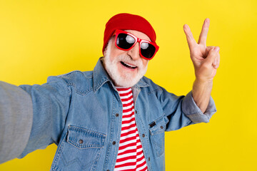 Poster - Self-portrait of elderly retired pensioner cheerful grey-haired man showing v-sign isolated over bright yellow color background