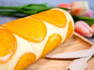 Wall Mural - Close up of orange cake roll with slice orange fruit on wooden plate.