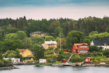 Wall Mural - Sweden. Beautiful Red And Yellow Swedish Wooden Log Cabins Houses On Rocky Island Coast In Summer Evening. Lake Or River Landscape