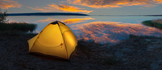 Wall Mural - orange tourist tent illuminated from the inside on the lakeside under dramatic sky