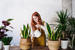 © Westend61 - Redhead woman pouring water in potted plant at home