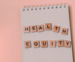 © Giedrius - Message health equity with wooden letters on notebook in pink.