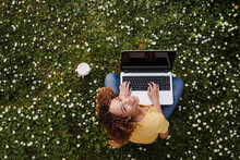 Young Woman Looking Up While Sitting With Laptop On Meadow Amidst Flowers