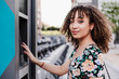 © Westend61 - Young woman with curly hair payment machine for bicycle sharing system