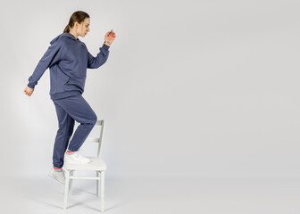 Full length portrait of young sporty fitness women in blue cotton hooded sweatsuit casual outfit playing with white chair. Studio shot of blonde Hoody woman with long hair in hoodie activewear set.