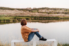 Senior Woman Looking At Mountains While Sitting On Bench Near Lake