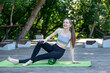 Happy smiling young slender woman kneads the muscles of the thighs with myofascial roller outdoors. Myofascial release.