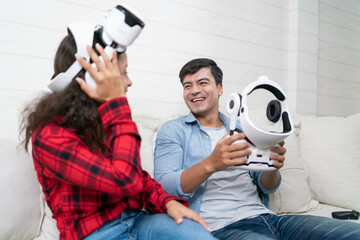 Excited Hispanic young couple wearing virtual reality headsets sitting on the couch enjoys playing games at home.