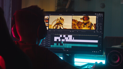 Teenager using computer to edit footage while sitting at desk in obscure room at night at home