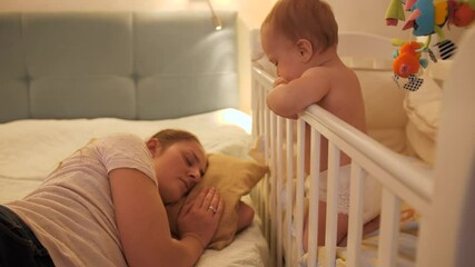 Wall Mural - Little crying baby boy waking up his mother sleeping in bed at night. Concept of parenting, parent fatigue and children development.