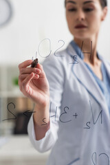 blurred scientist writing chemical formulas with felt pen on glass board.