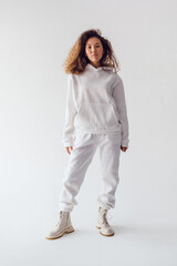 Wall Mural - Attractive woman with thick curly hair in a white suit of hoodies and sweatpants. Mock-up.