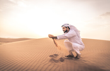 Wall Mural - Arabic man with traditional emirates clothes walking in the desert