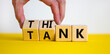 Think tank symbol. Businessman turns wooden cubes and changes the word 'tank' to 'think' or vice versa. Beautiful yellow table, white background, copy space. Business, think tank concept.