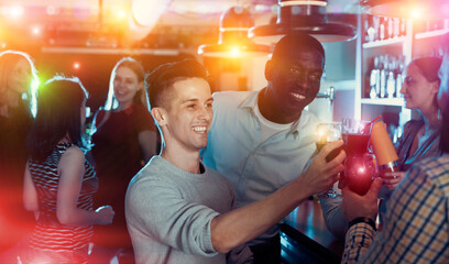 Wall Mural - Happy men friends with glasses of cocktails chatting at night club