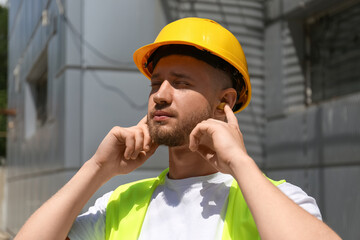 Male worker putting ear plugs outdoors