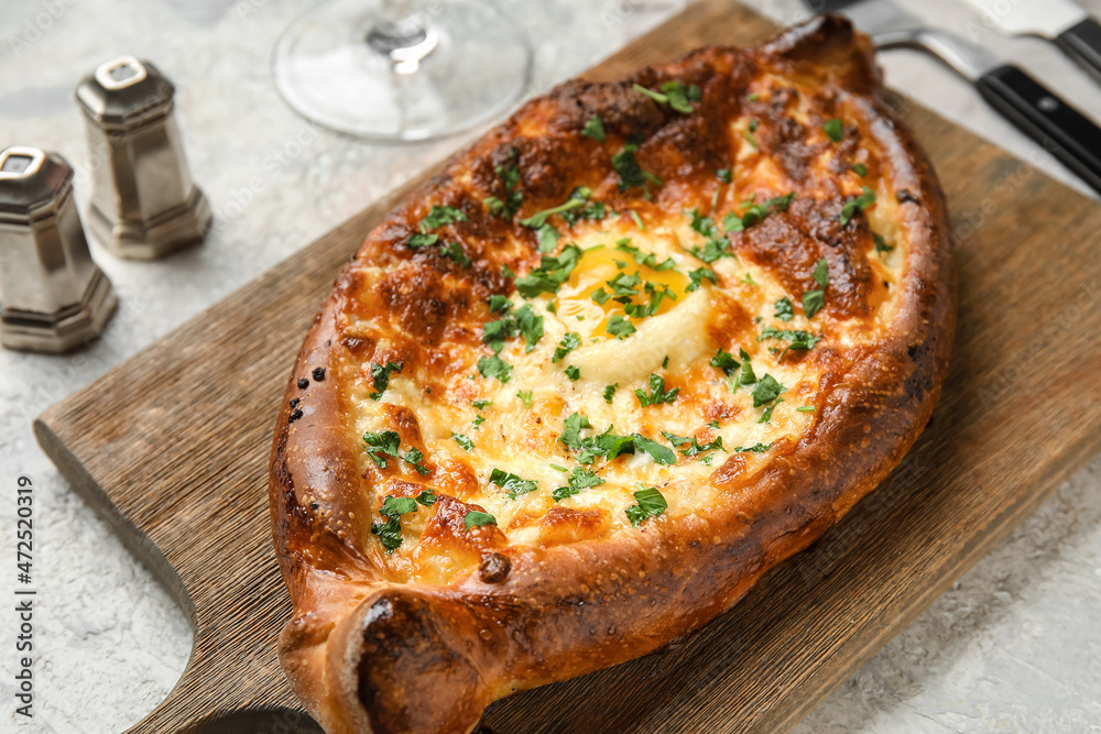 Tasty Ajarian khachapuri served on wooden board, closeup