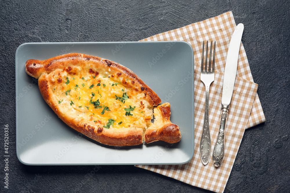 Plate with tasty Ajarian khachapuri on dark table background