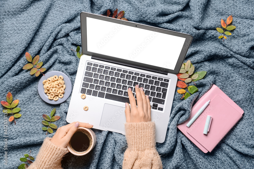 Woman with cup of coffee using laptop on grey fabric background