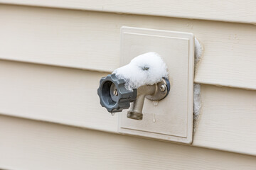 Outdoor water spigot covering in snow during winter. Home repair, maintenance and weatherproofing concept.