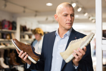 Wall Mural - Interested male shopper choosing comfortable casual shoes, comparing two moccasins models in store