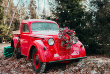 Red Car Pickup Truck Decorated With Christmas Wreath, Blankets, Pillows And Gift Boxes With Presents Is Standing In Forest, Santa Claus's Magic Transport, New Year And Christmas Banner Background