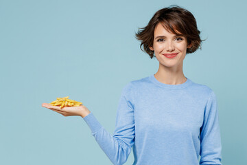 Wall Mural - Young smiling woman wearing casual sweater looking camera hold in palm hand fastfood french fries potato isolated on plain pastel light blue background studio portrait. People lifestyle food concept.