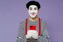 Smiling Amazing Marvelous Ecstatic Young Mime Man With White Face Mask Wears Striped Shirt Beret Hold In Hand Use Mobile Cell Phone Isolated On Plain Pastel Light Violet Background Studio Portrait
