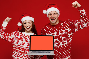 Wall Mural - Young couple friends two man woman in sweater hat hold use work on laptop pc computer blank screen workspace area do winner gesture isolated on plain red background studio Happy New Year 2022 concept