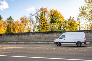 Compact mini van for commercial use and small business running on the road with autumn yellow trees on the side