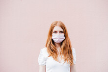 Redhead Woman Wearing Protective Face Mask While Standing In Front Of Pink Wall During COVID-19