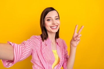 Wall Mural - Portrait of cheerful pretty girl take selfie fingers make v-sign hello greetings symbol isolated on yellow color background