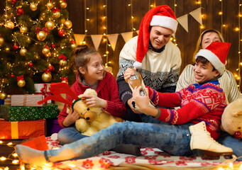 Wall Mural - Happy family posing in new year or christmas decoration. Children and parents. Holiday lights and gifts, Christmas tree decorated with toys.